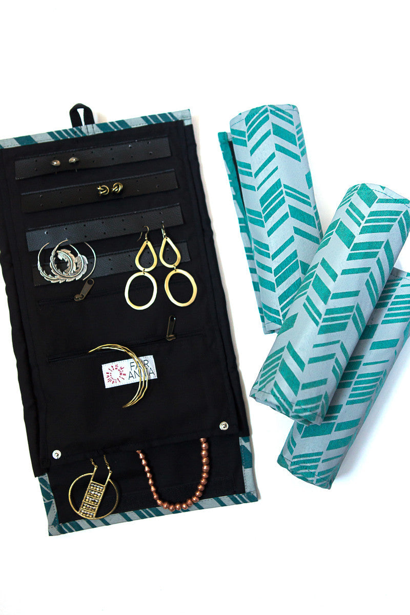 A green jewelry roll travel case with chevron pattern, unrolled to show compartments for earrings, rings, and necklaces, with jewelry items like earrings, rings, and necklaces organized within it.