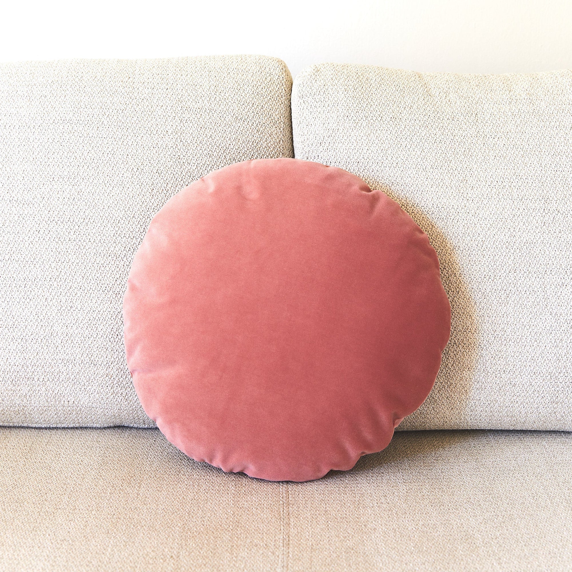 Pink circular pillow on a beige couch