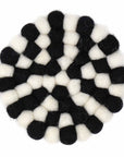 A circular felt coaster with a geometric pattern of black and white pom-poms