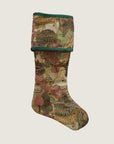 A reversible holiday stocking with a tapestry design featuring geometric patterns and festive colors like green, red, and beige, finished with green velvet piping