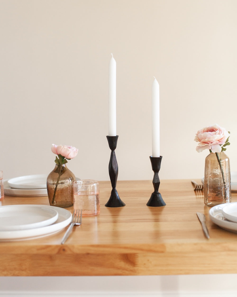 Dining table setting with black candlesticks, pink flowers, and glassware.