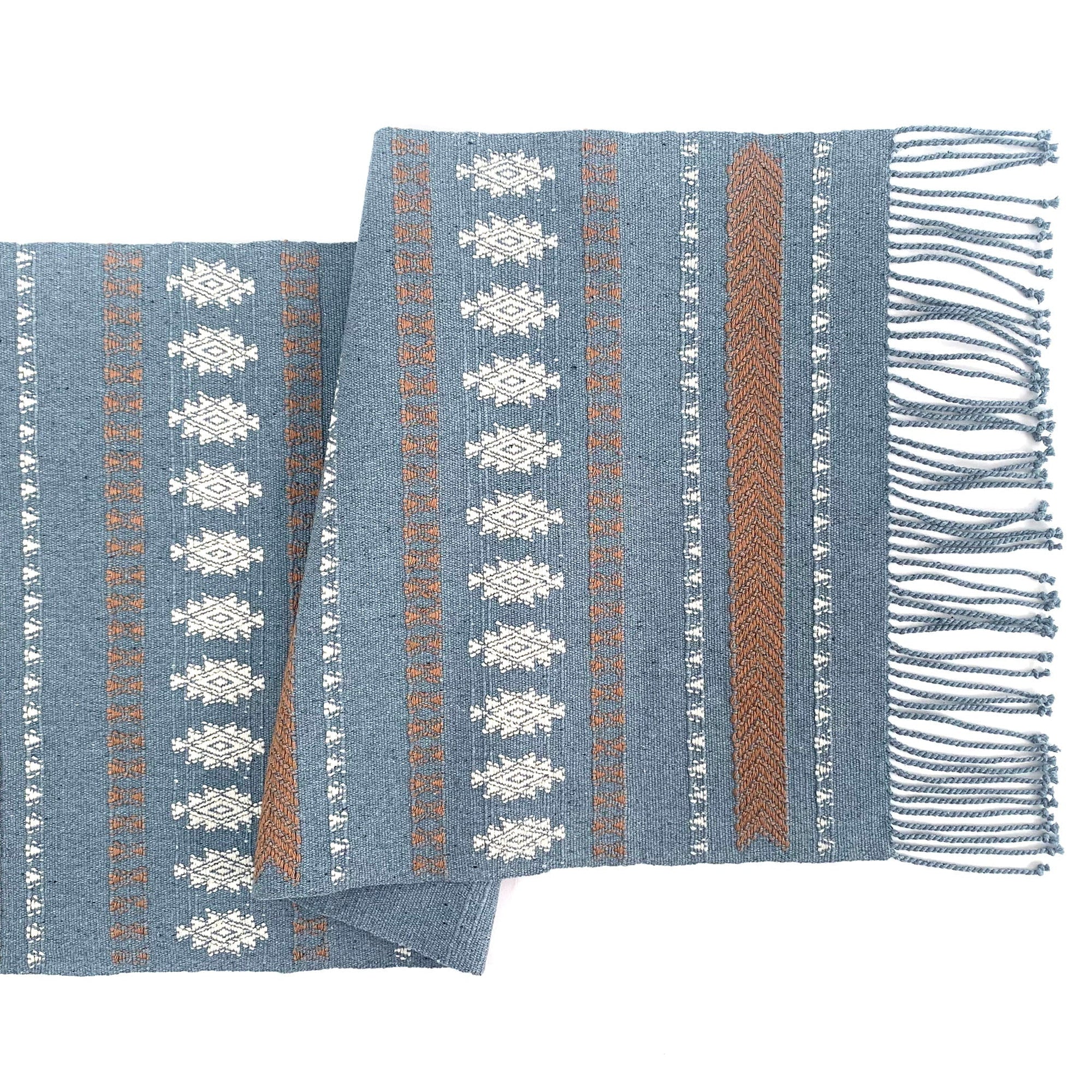 Blue woven blanket with pattern and fringes on a white background