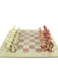 A hand-carved soapstone chess set with a green and pink checkered board and beige, pink, and white stone pieces.