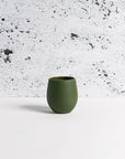 A matte green stoneware coffee cup placed against a textured white background
