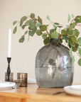 Decorative setting with a vase of greenery, candle, and cutlery on a table.