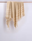 Beige towel with fringes hanging on a wooden rod against a white wall