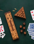 Triangle solitaire peg board game with the pegs inside on a green background next to dice, cards, and a cribbage board.