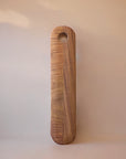 A long, smooth, brown wooden cutting board with a hole near the top for hanging