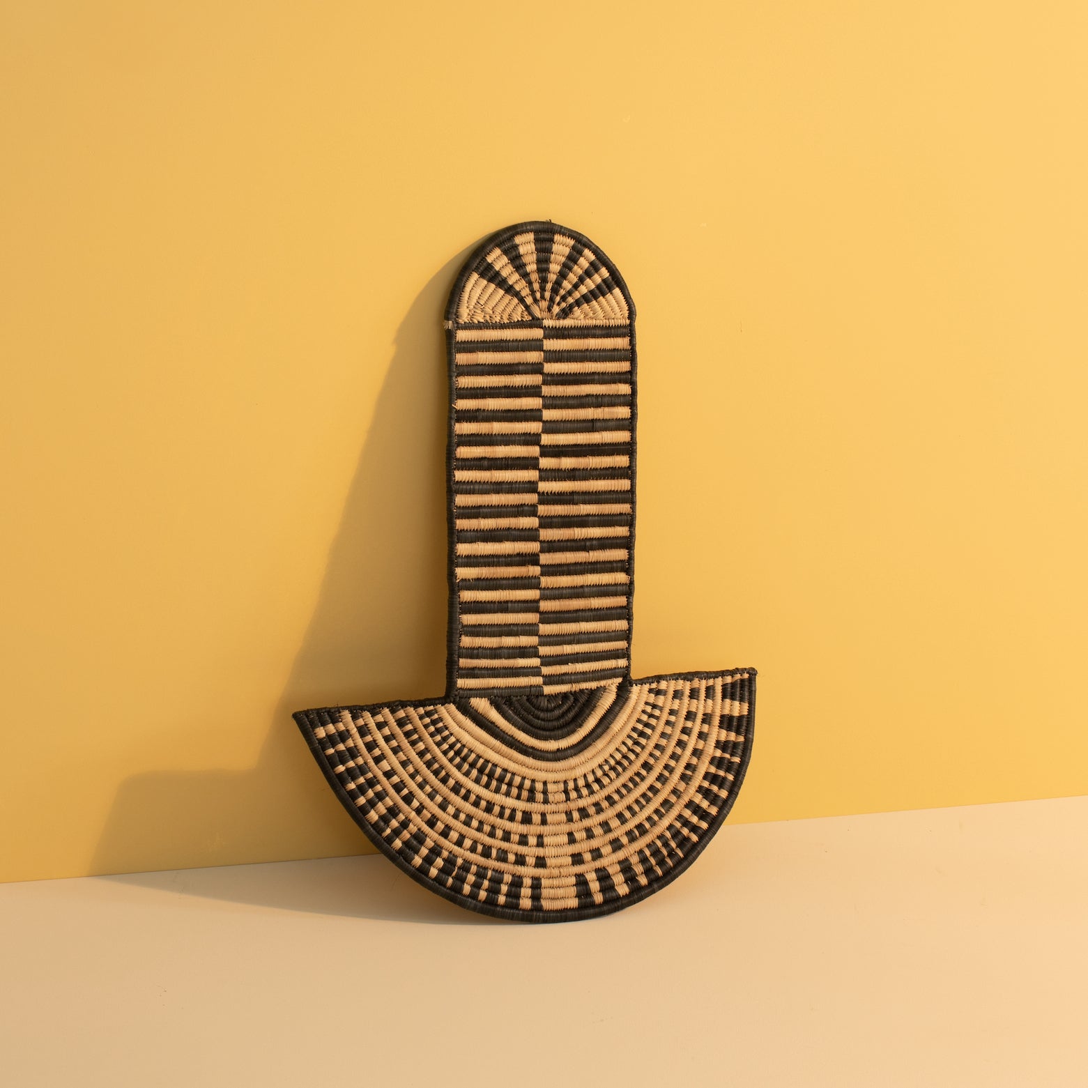 A woven abstract wall mask with geometric patterns, inspired by traditional African masks, placed against a yellow background