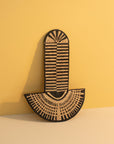 A woven abstract wall mask with geometric patterns, inspired by traditional African masks, placed against a yellow background