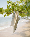 A beige and blue striped Turkish towel hanging on a tree branch with the ocean in the background