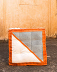 Floor cushion with orange border and striped pattern on a stone floor against a beige wall