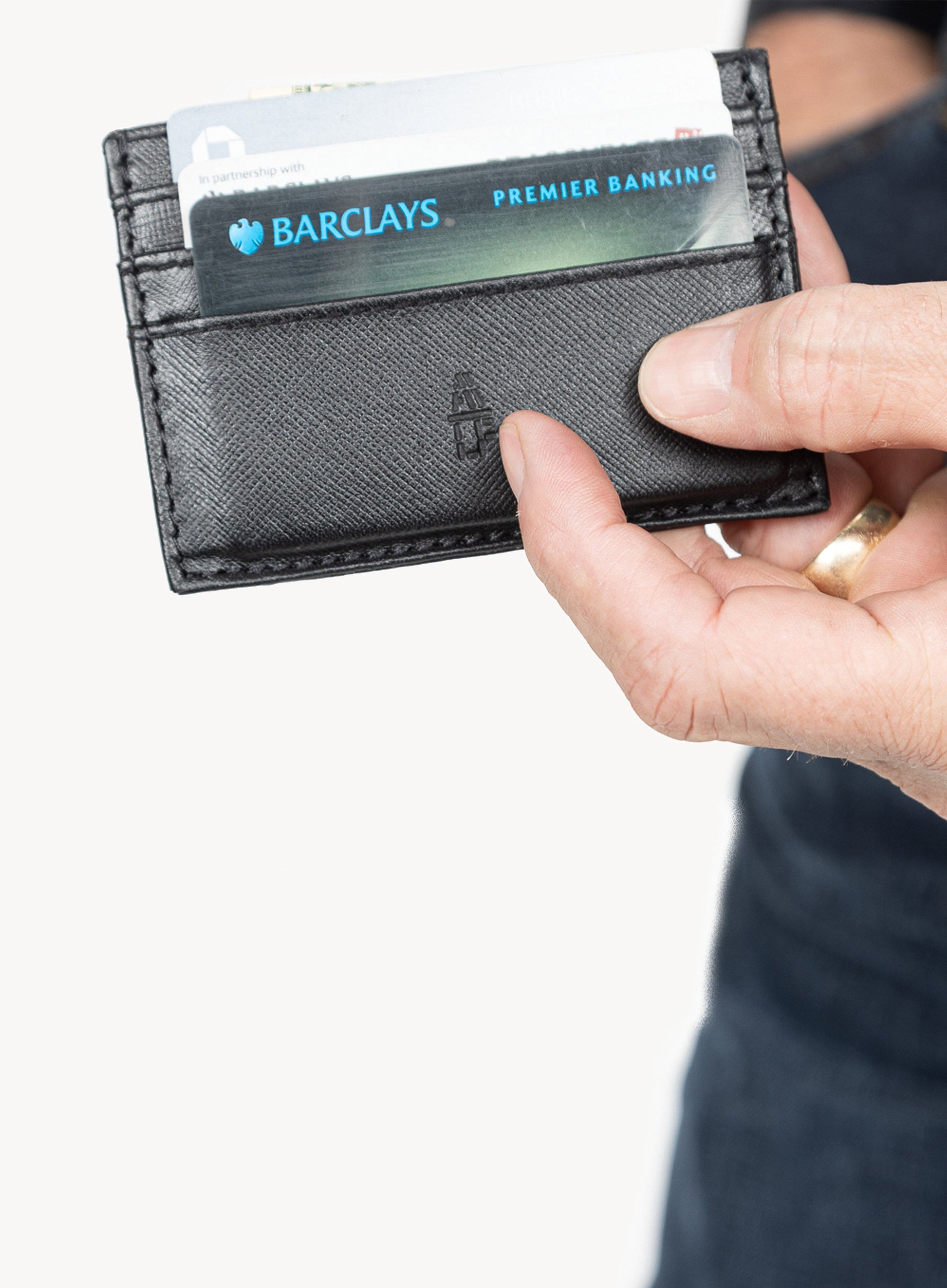 Person holding a black wallet with a Barclays card inside on a white background