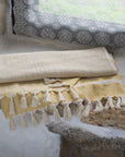 Yellow towel with tassels on a stone surface, with a patterned pillow in the background