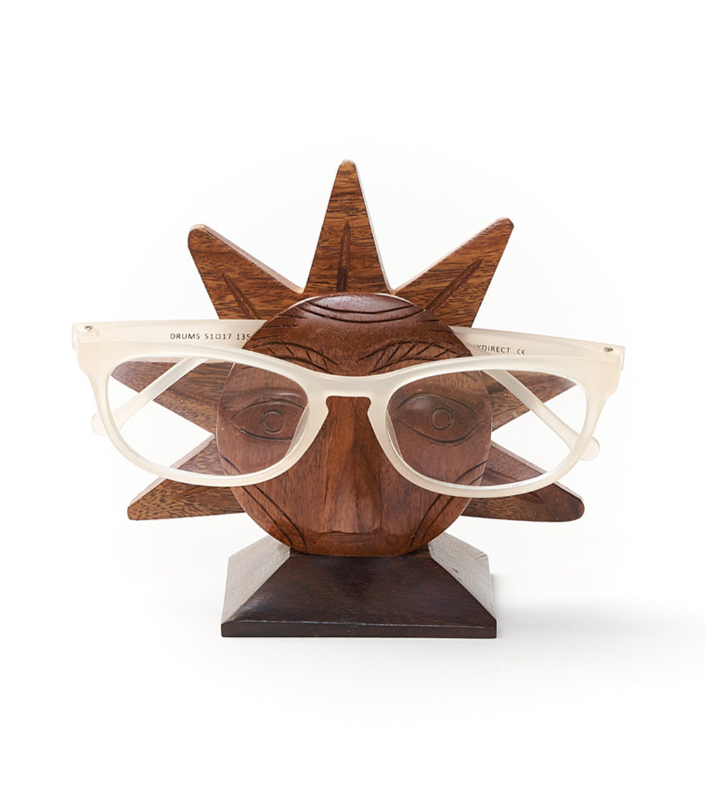 A wooden eyeglass holder stand with a sun face design, holding a pair of eyeglasses.