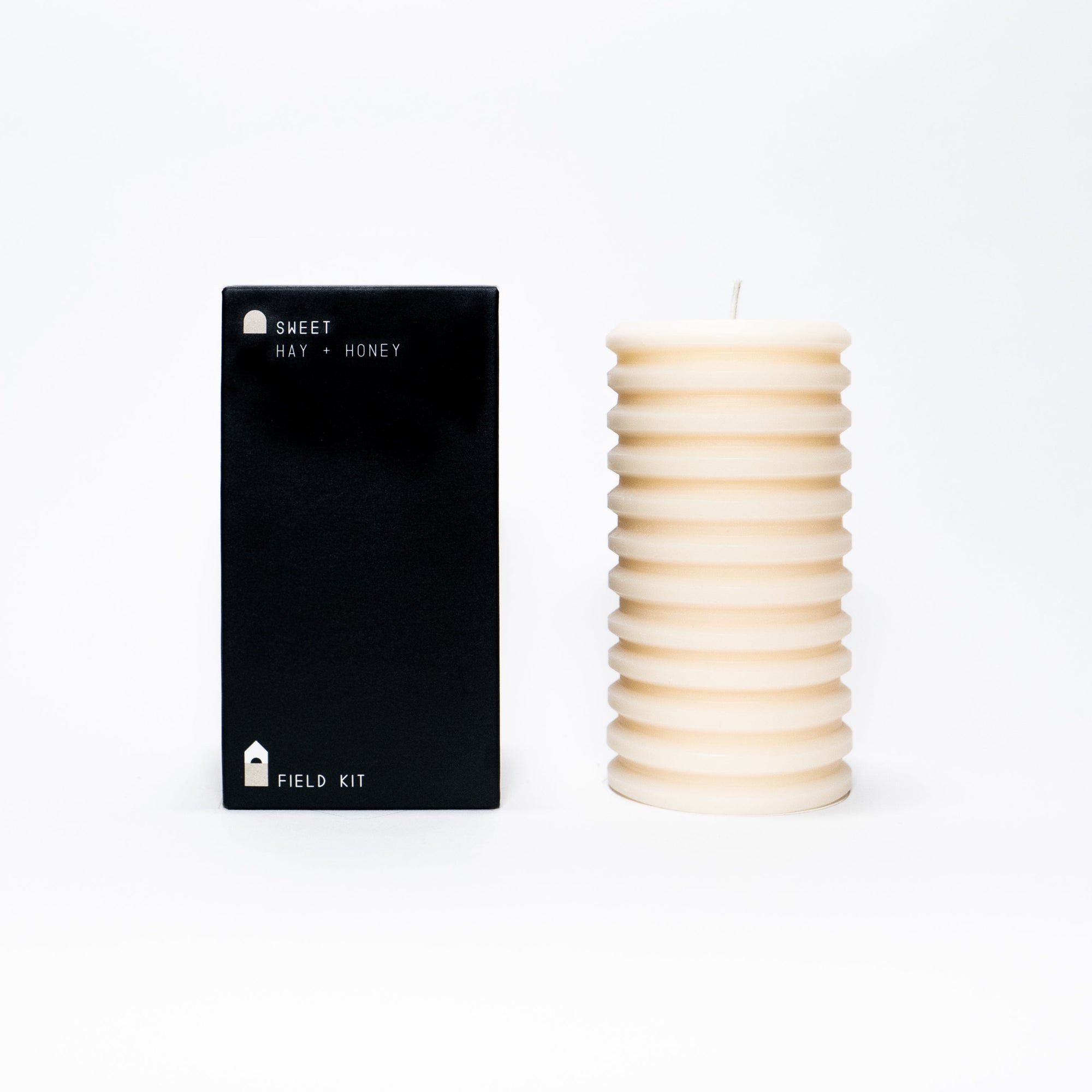 A sculptural pillar candle alongside its packaging, with the candle displayed on the right and the packaging labeled 'SWEET HONEY' from Field Kit.