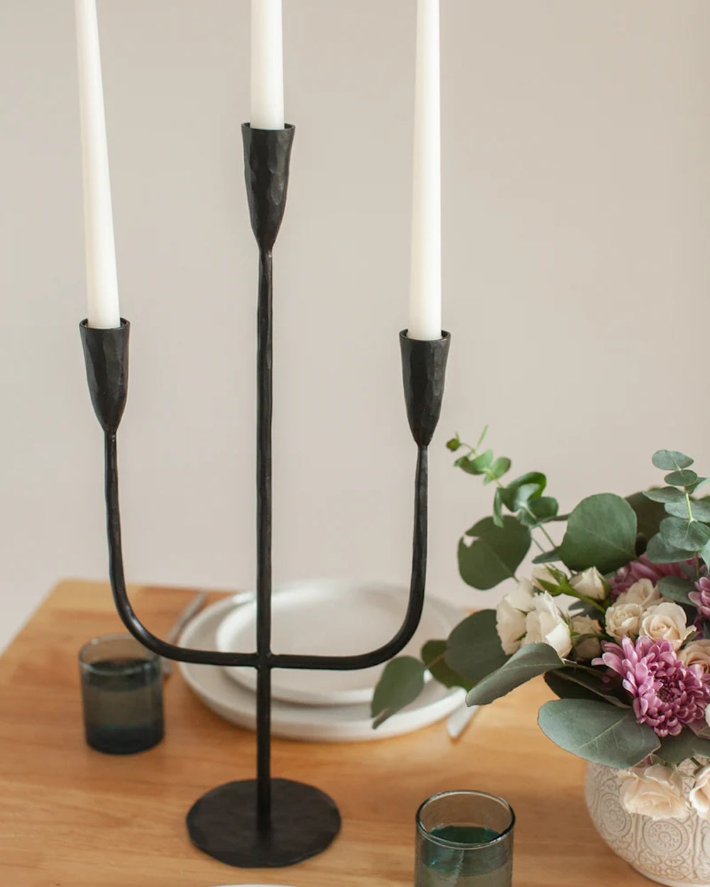 Black metal candle holder with three white candles on a table.