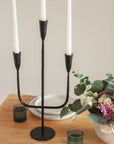 Black metal candle holder with three white candles on a table.