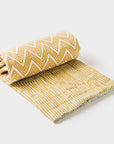 A rolled-up yellow and white striped throw with a zigzag pattern, partially unrolled to show the texture and design