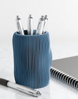 Blue textured pen holder with pens and a notebook on a white surface