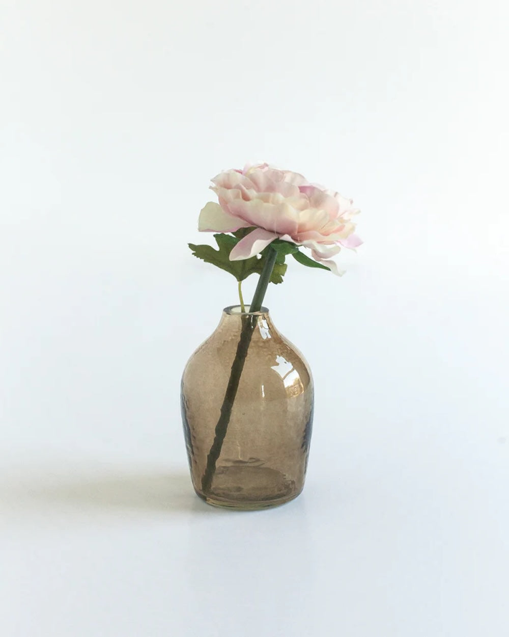 Small brown glass vase with a single pink flower on a white background