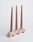 A beige wavy candelabra made of soapstone, holding three vertical candles.