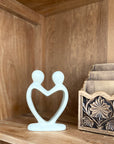 A handmade stone sculpture depicting two figures holding hands on a wooden shelf