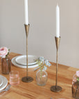 Gold candle holders on a table with plates and flowers.