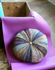 Colorful round yoga pillow on a pink yoga mat with a wooden floor background