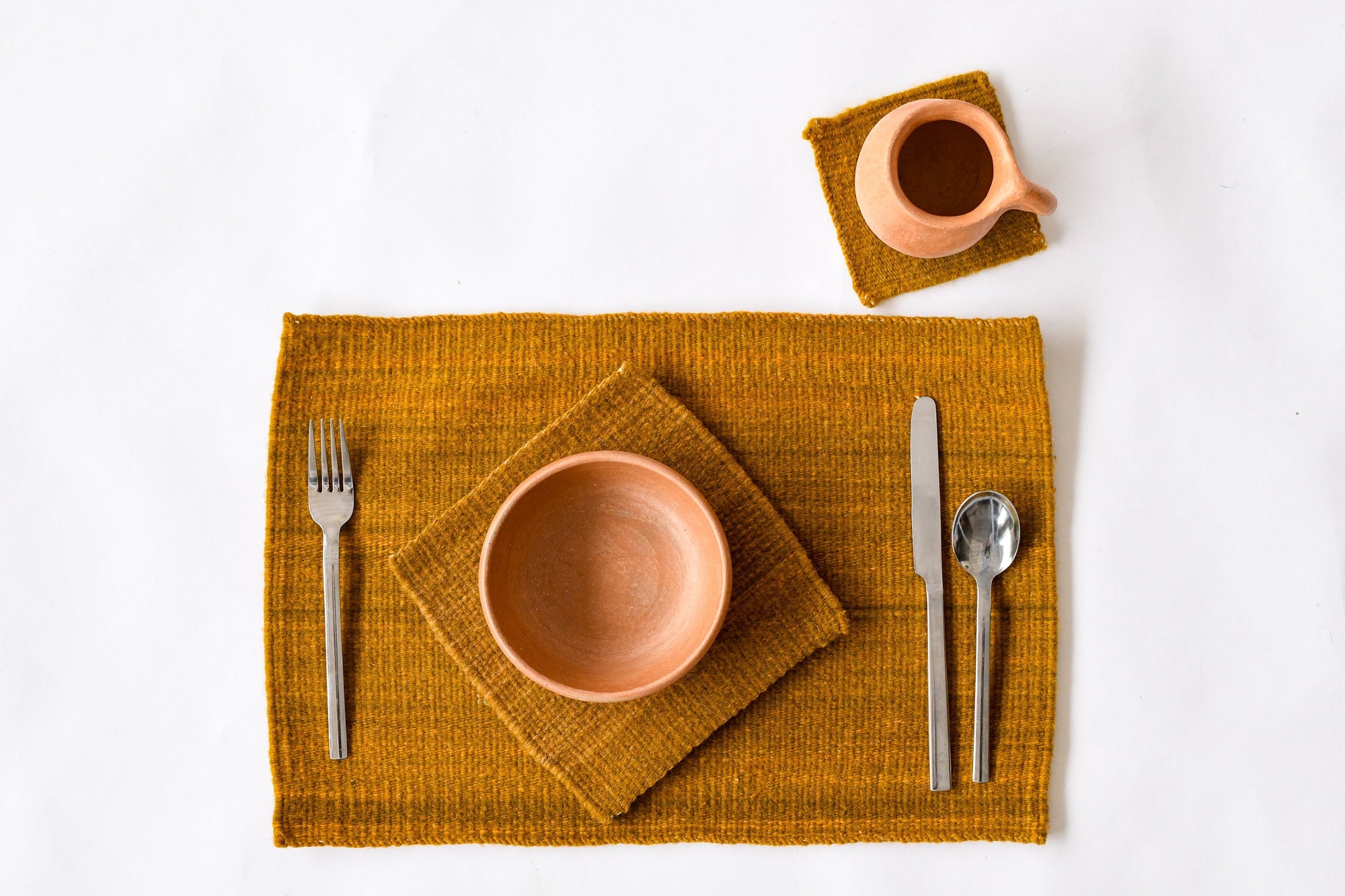 Ceramic tableware including a bowl, cup, fork, knife, and spoon on a wool placemat and wool trivet