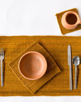 Ceramic tableware including a bowl, cup, fork, knife, and spoon on a wool placemat and wool trivet