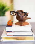 A handcarved Indian rosewood glasses stand shaped like a bird perched on a base on top of a set of books