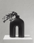 A black, handmade ceramic vase holding purple flowers