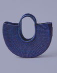 A hand-dyed blue, half-moon shaped handbag made from elephant grass, with an open top and two handles.