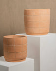Two terracotta pots with a geometric pattern on a white pedestal against a beige background