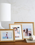 Three wooden picture frames with photos on a table next to a lamp.