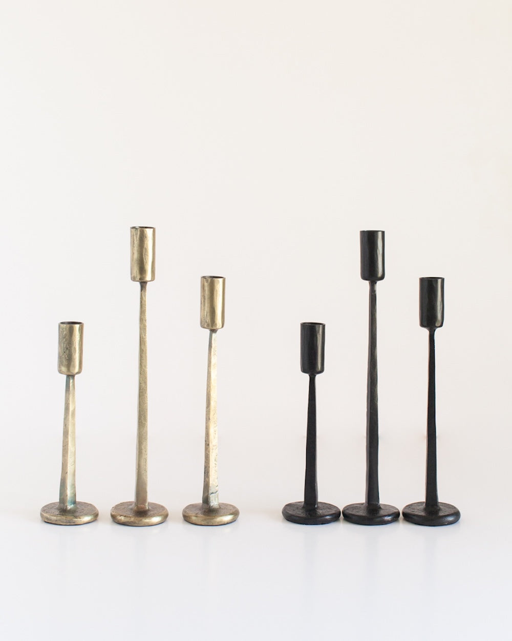Two sets of three candle holders in brass and black on a white background