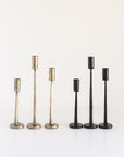 Two sets of three candle holders in brass and black on a white background
