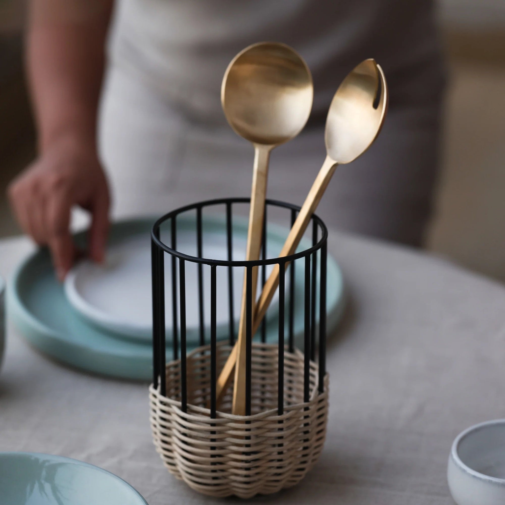 A pair of brass salad server in a black wire holder on a table with a blurred background