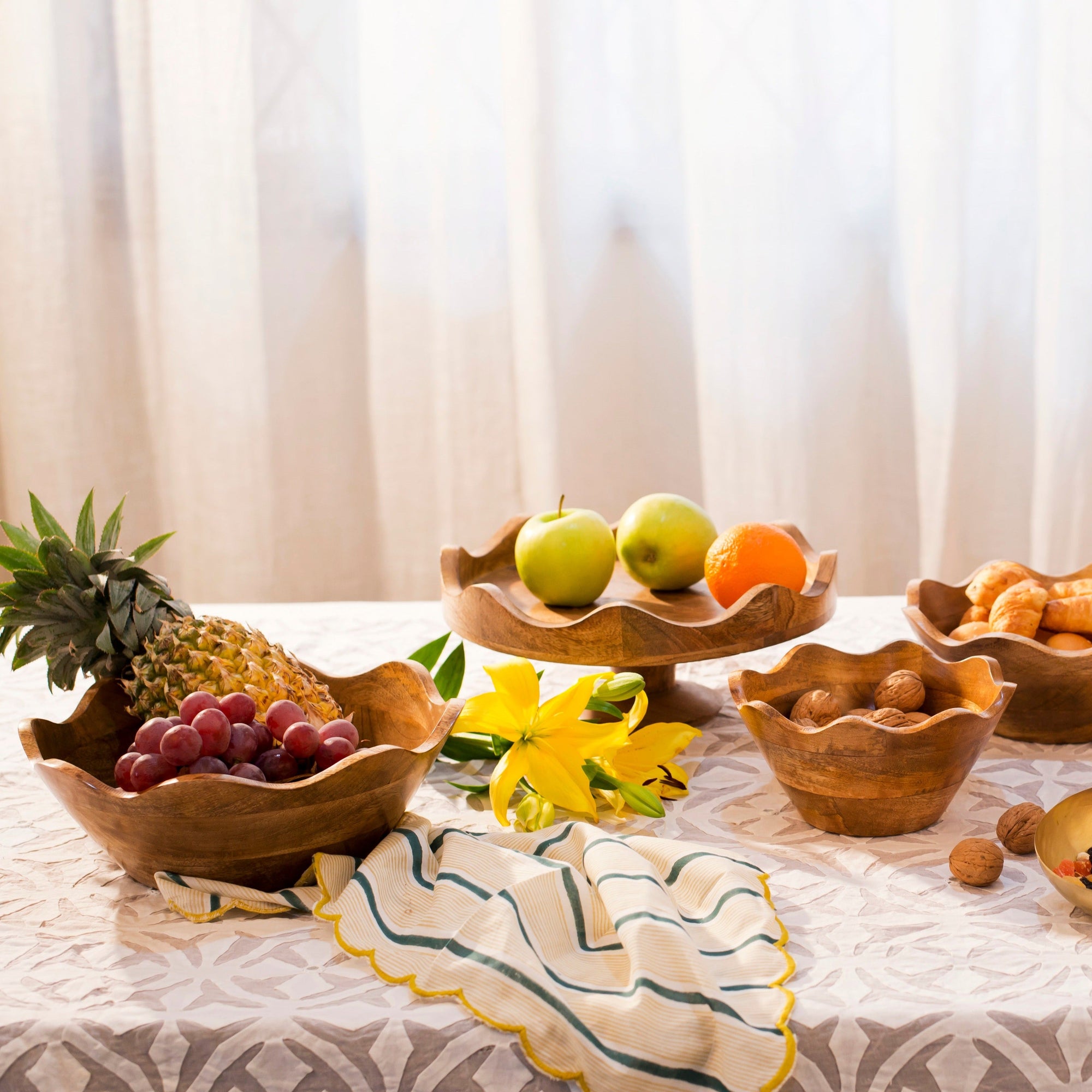 Wooden bowls with fruits and snacks on a table with a light curtain background