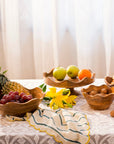 Wooden bowls with fruits and snacks on a table with a light curtain background