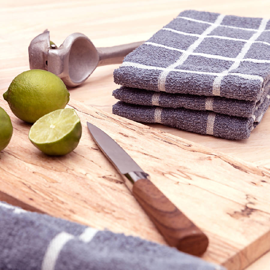 Two terry kitchen towels on a wooden cutting board next to a knife and limes