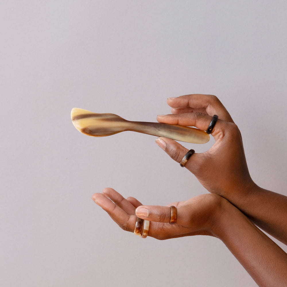 A pair of hands holding a horn butter and cheese spreader with a light beige color