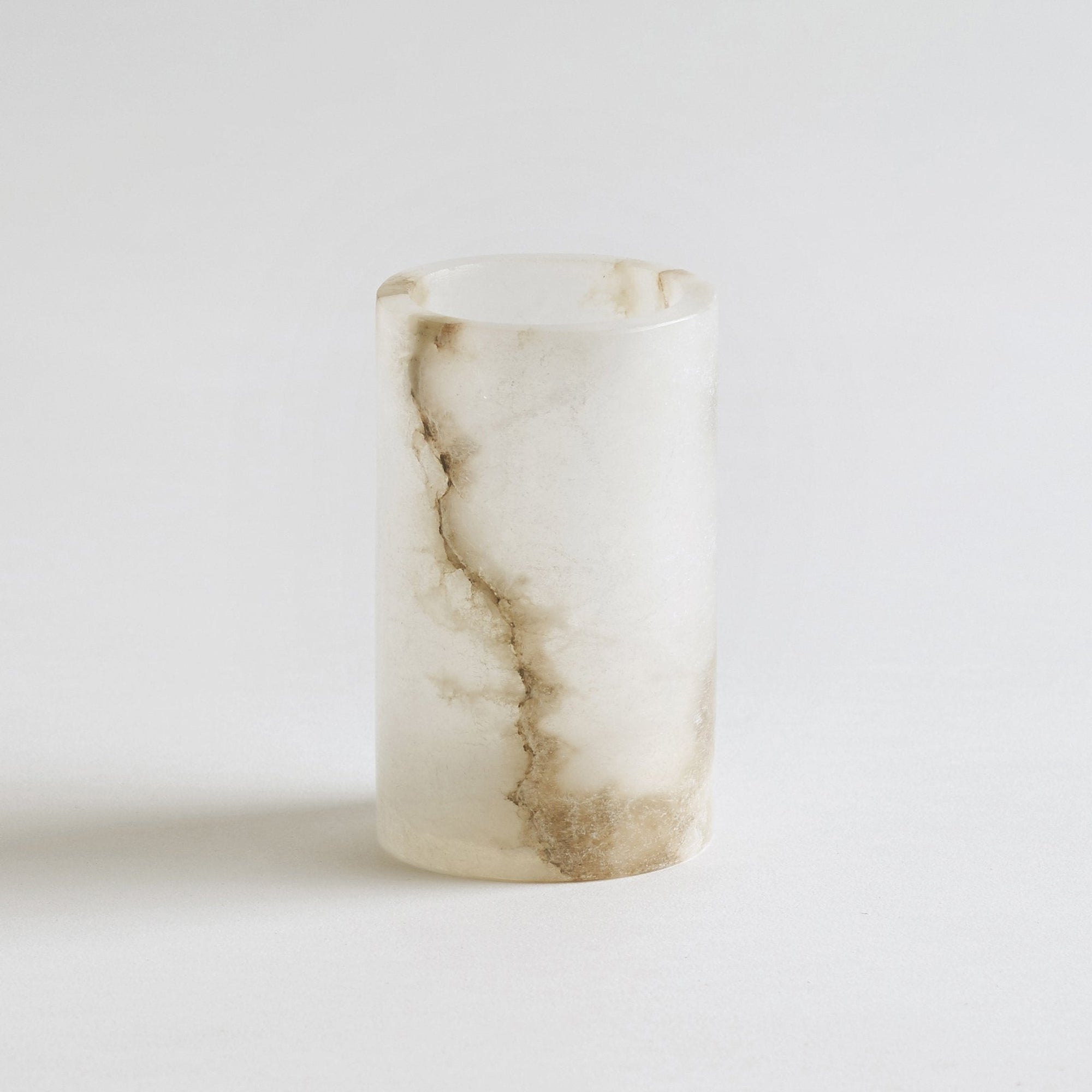 A hand-cut alabaster tealight holder with a cylindrical shape, displaying natural white and beige swirls and bands of color