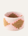 A handwoven trinket basket with pink and tan colors, circular base, and tightly coiled pattern.