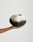 Hand holding a black and white decorative wool bowl against a plain background