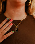 A model wearing a gold-plated pendant necklace with a rectangular black enamel pendant featuring a white star and moon pattern, connected to a chain by a small gold-plated bar.