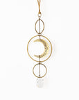 A brass suncatcher with a crescent moon design, consisting of gold-colored metal rings and a white crystal pendant, hanging against a white background.