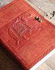 Red leather-bound book with an embossed elephant design on a wooden surface