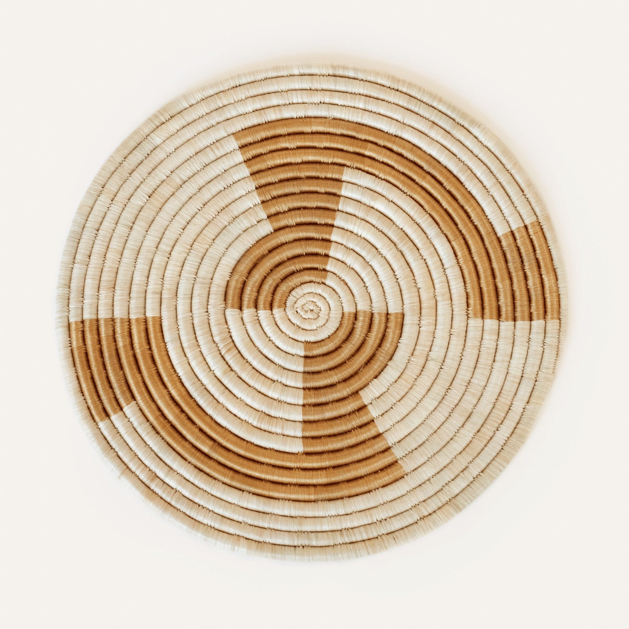A round placemat featuring geometric patterns in natural and gold colors, handwoven from raffia and sisal fibers